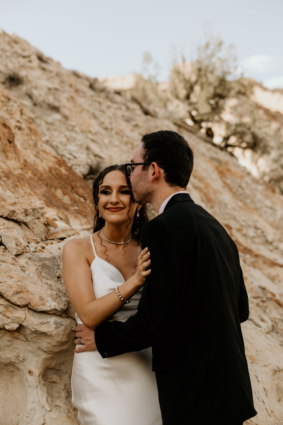 bride and groom leaning on a rock hugging