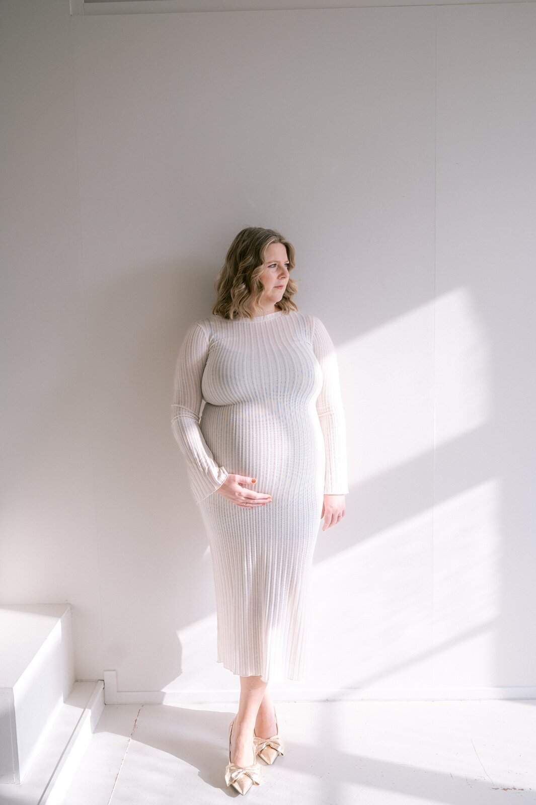 Zwangere vrouw poseert voor een witte studio muur met schaduw muur.