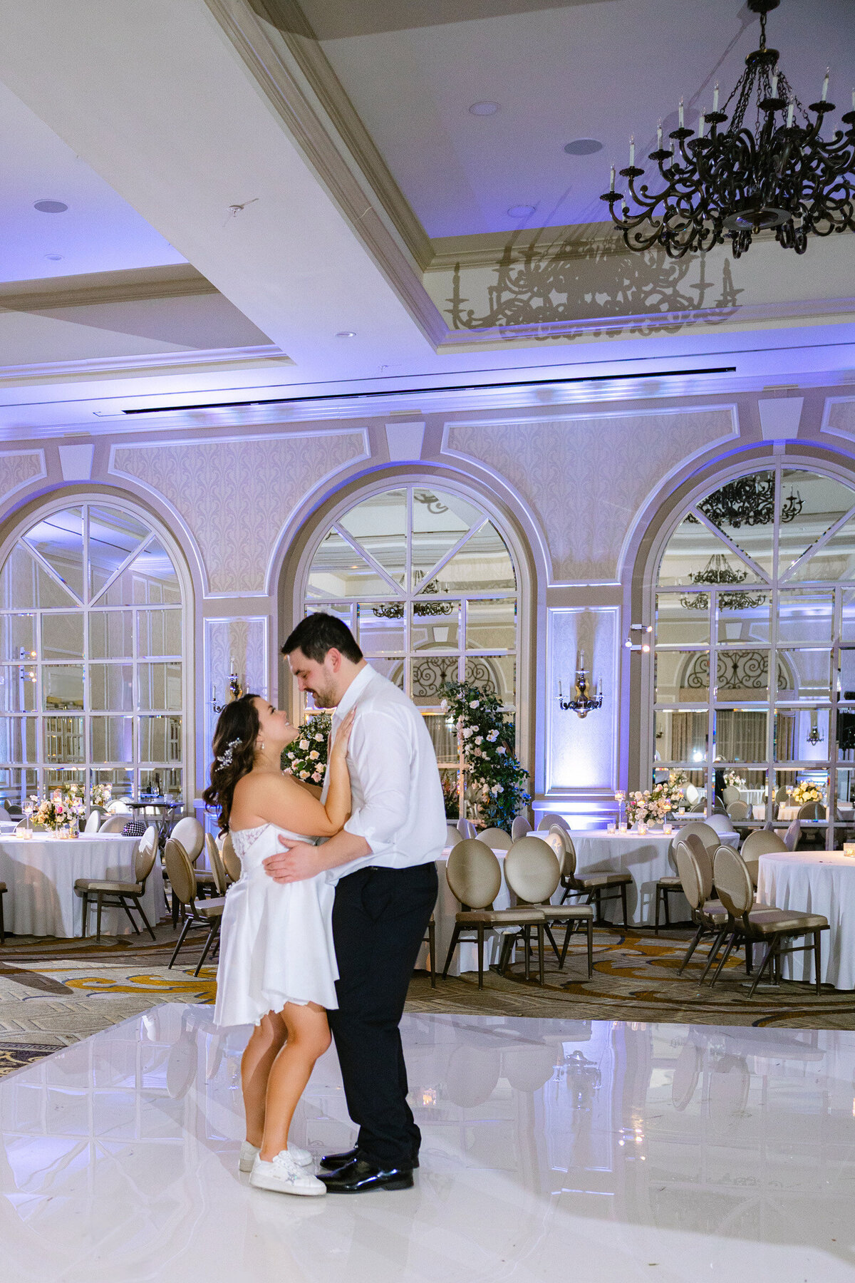 bride and groom during their last private dance elegantly styled wedding reception table at The Adolphus in Dallas featuring a black tablecloth, tall glass vases with pink rose arrangements, numerous candles, and refined glassware and chargers