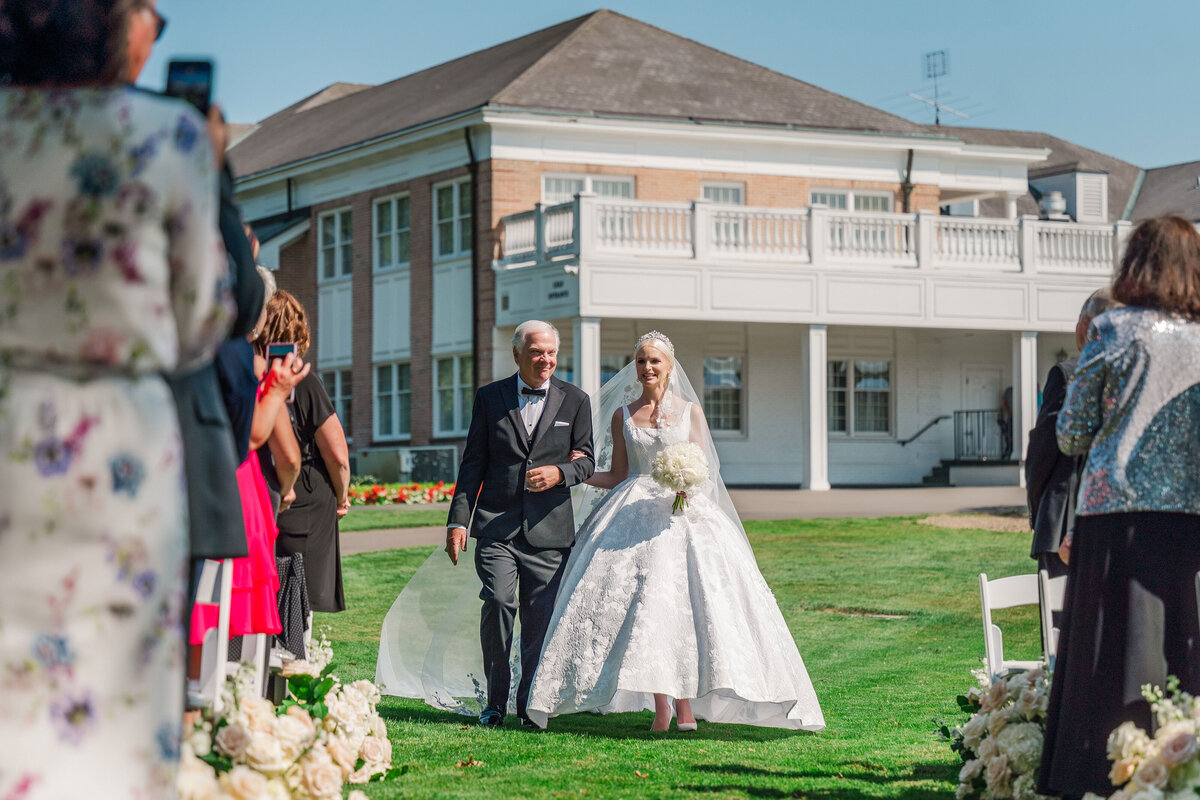 bride and her dad walking down the aisle in the sunshine during her wedding ceremony at The Grand Resort