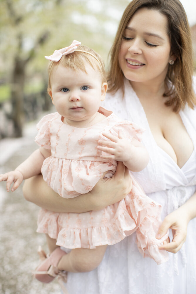 mom holding young daughter in pink dress during park family portraits