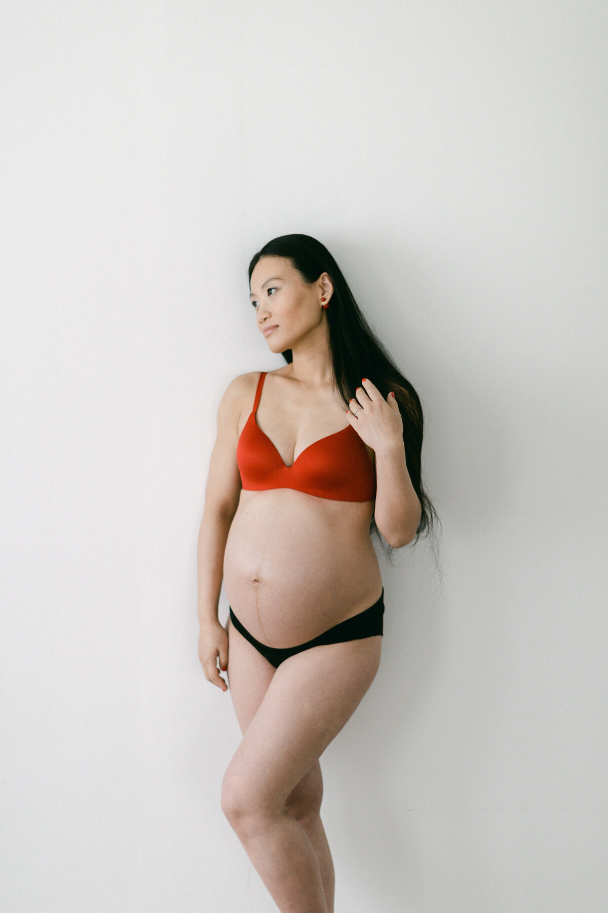 Asian woman in red bra showing her pregnant belly during maternity session