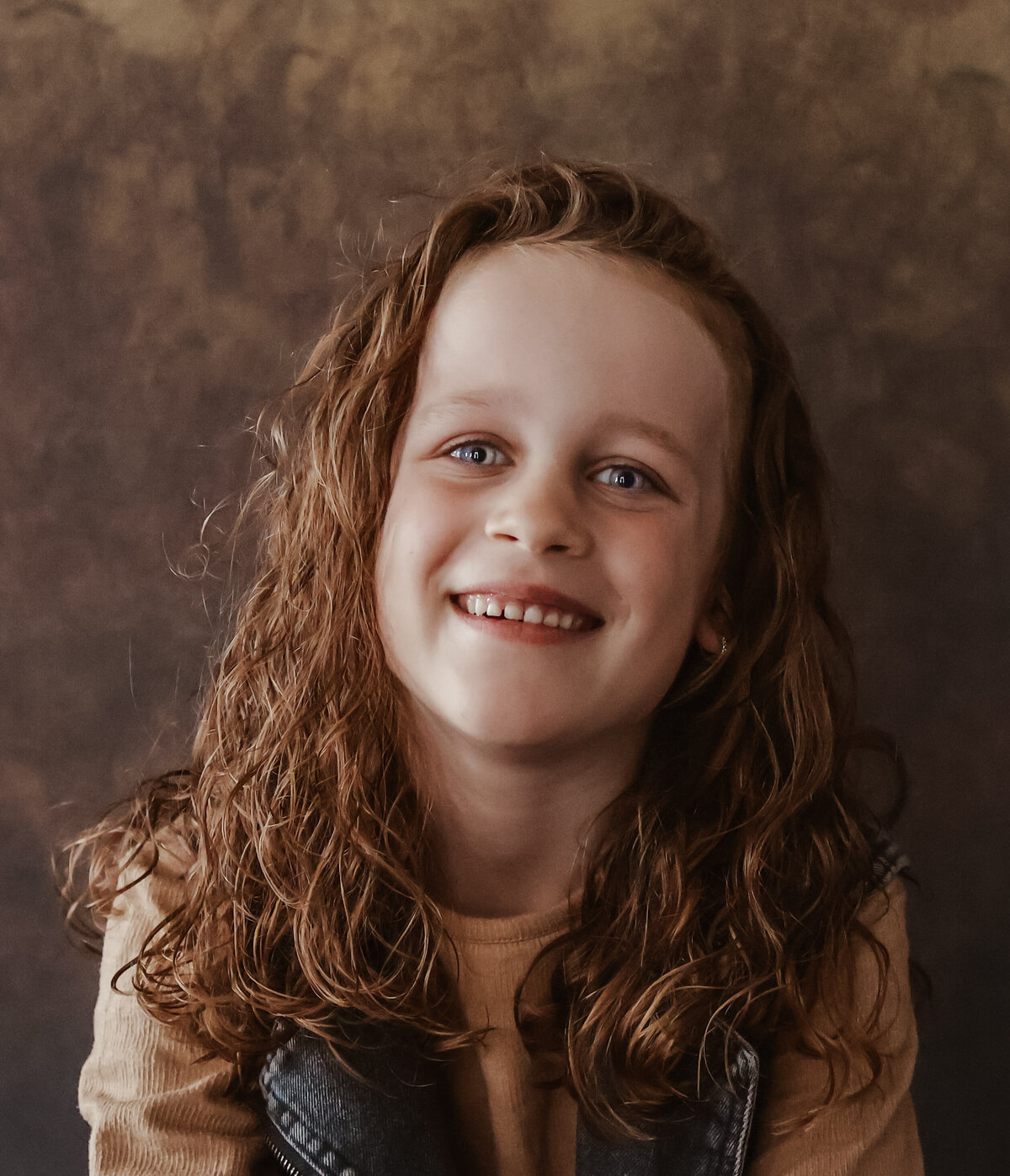 Een vrolijk meisje met krullen, portret gefotografeerd tegen een lichtbruine achtergrond