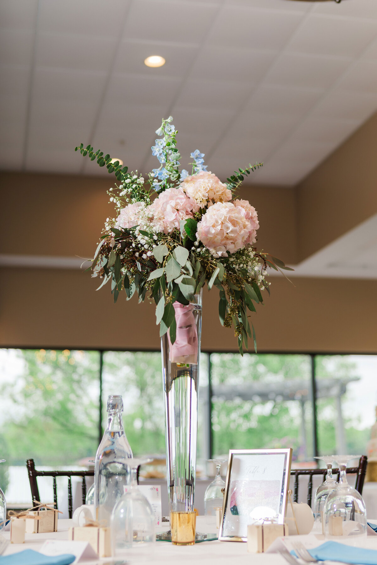 tall wedding centerpiece with hydrangeas and blue flowers adorning a table at vineyards at pine lake event center