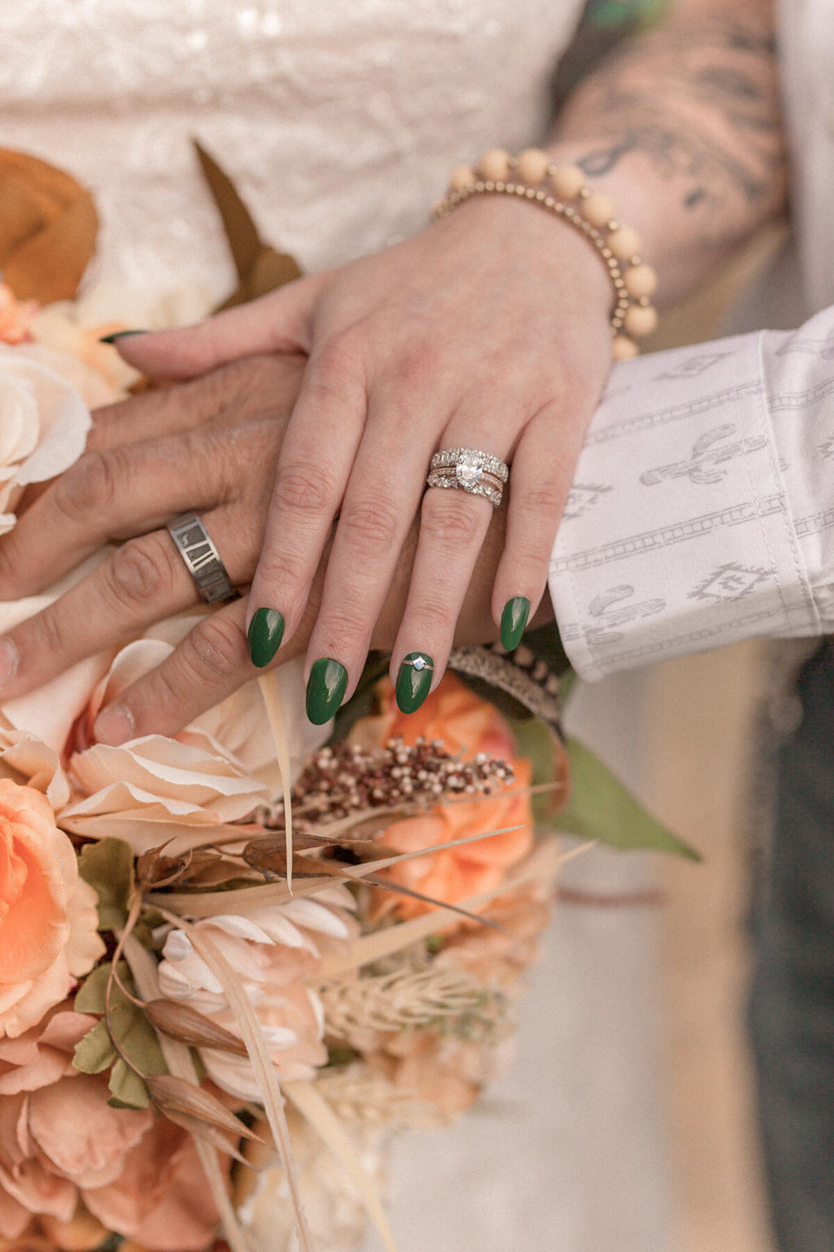 A close up image of the bride and groom's hands featuring their wedding bands, and the brides emerald green nails.