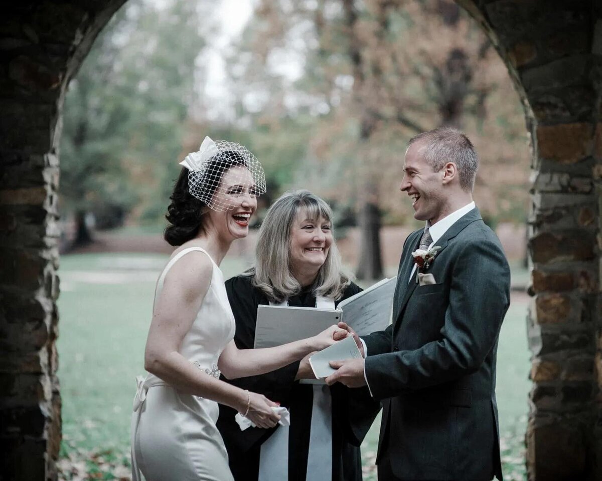 A bride and groom standing up with an officiant