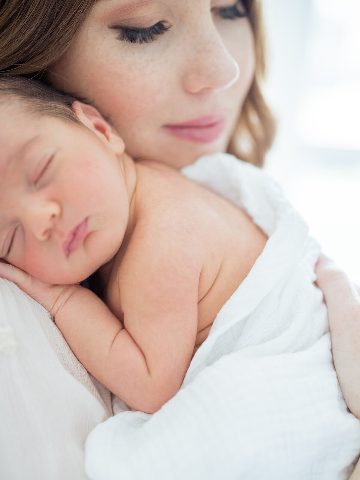Close-up image of baby boy sleeping on his mother's chest as she closes her eyes holding him.