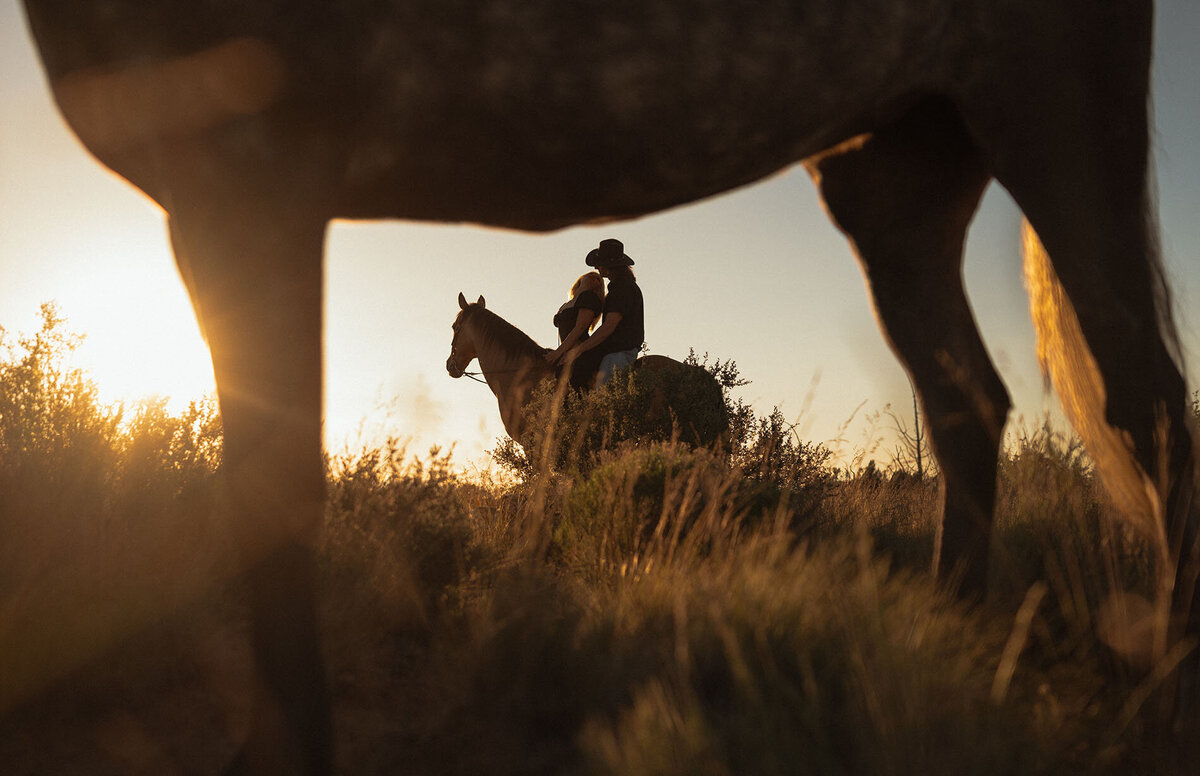 romantic golden hour portrait of engaged couple riding their horse, with warm sunset light
