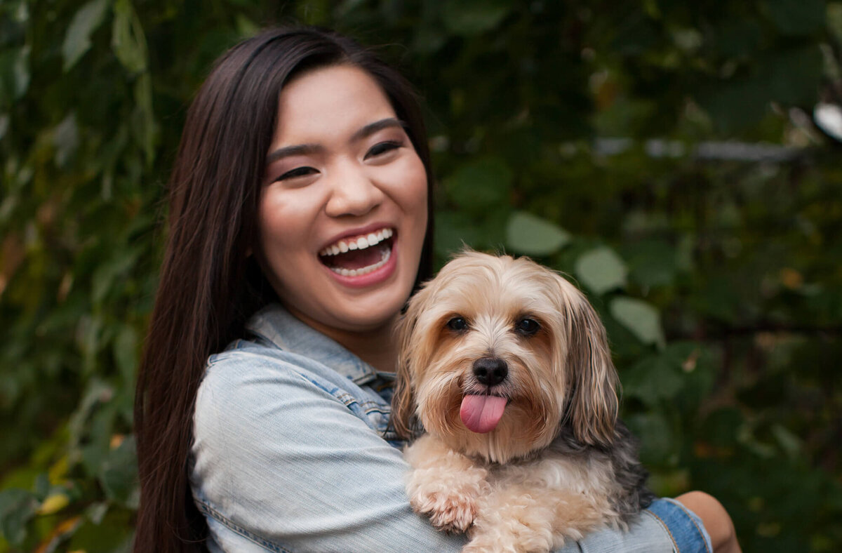 A senior girl laughs while holding her small family dog. Captured by Springfield, MO senior photographer Dynae Levingston.