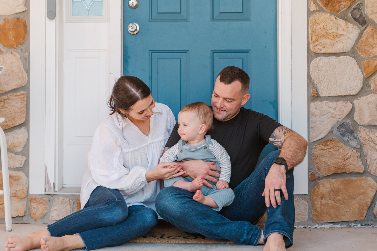 mom dad and one year old son sitting on their front porch in front of their blue door by harrisburg pa photographer