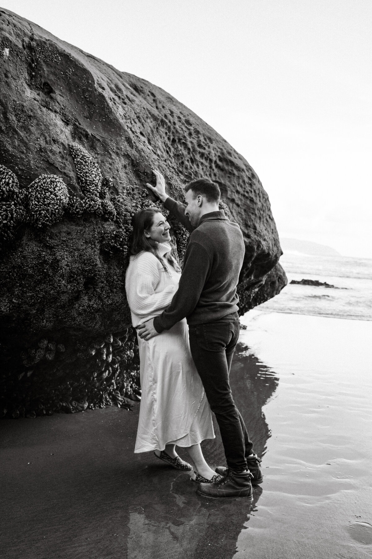 engaged couple leaning on a rock on the beach by photographers in idaho