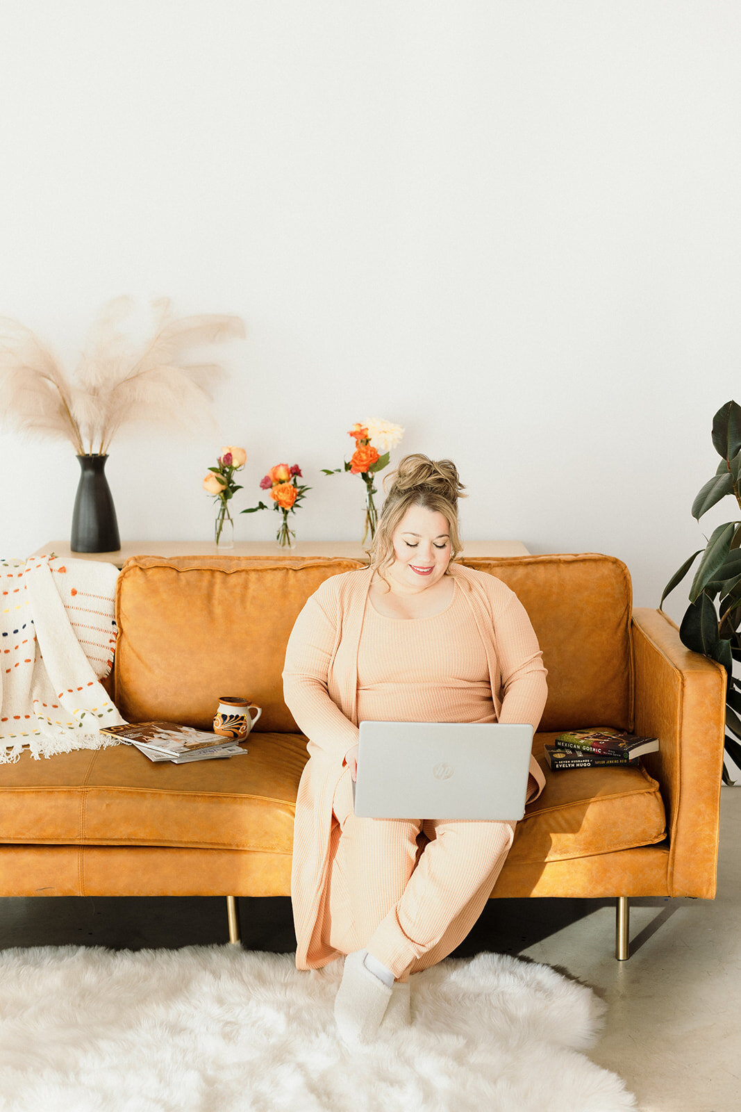 woman sitting on orange couch with her laptop and working with small smile
