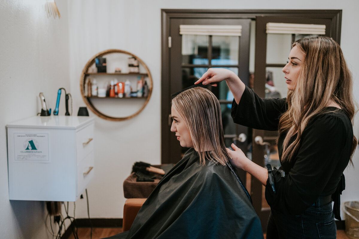 Camera takes a side angle shot of hair dresser talking with client about styling.