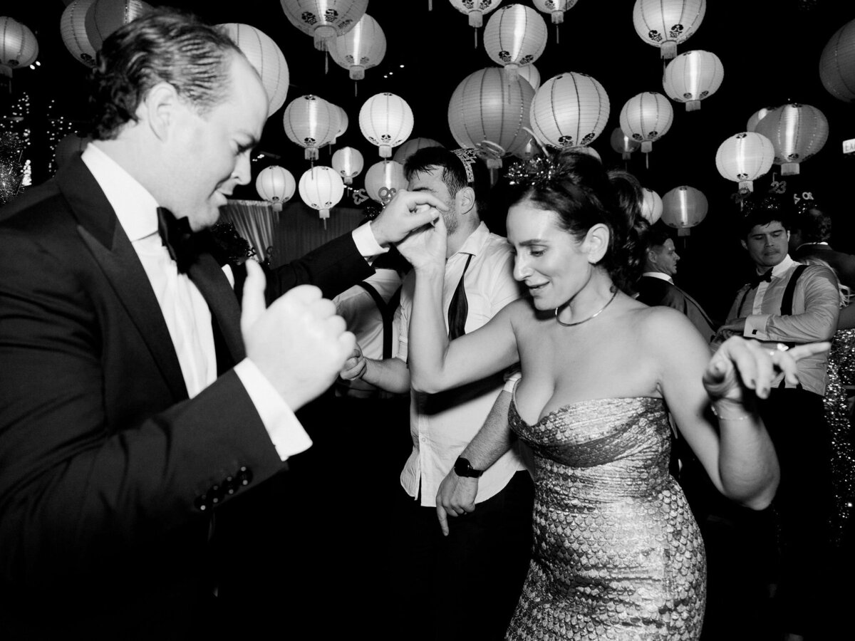 Wedding guests joyfully dance under a canopy of hanging lanterns, celebrating late into the night.