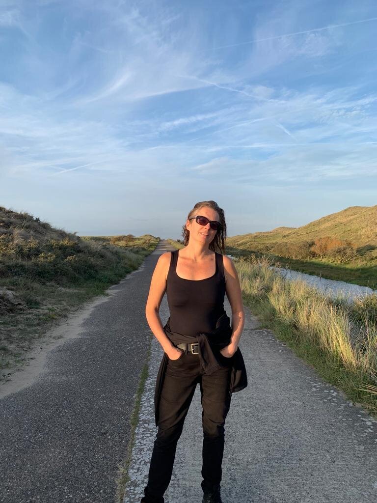Femke with sunglasses stands in the dunes of Amsterdam with hands in her pockets
