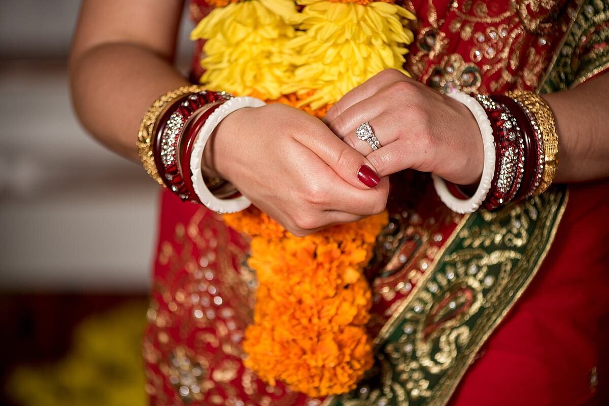 Indian Bride wearing gold, red and silver bangles and a yellow and orange varmala with her red, gold and green saree