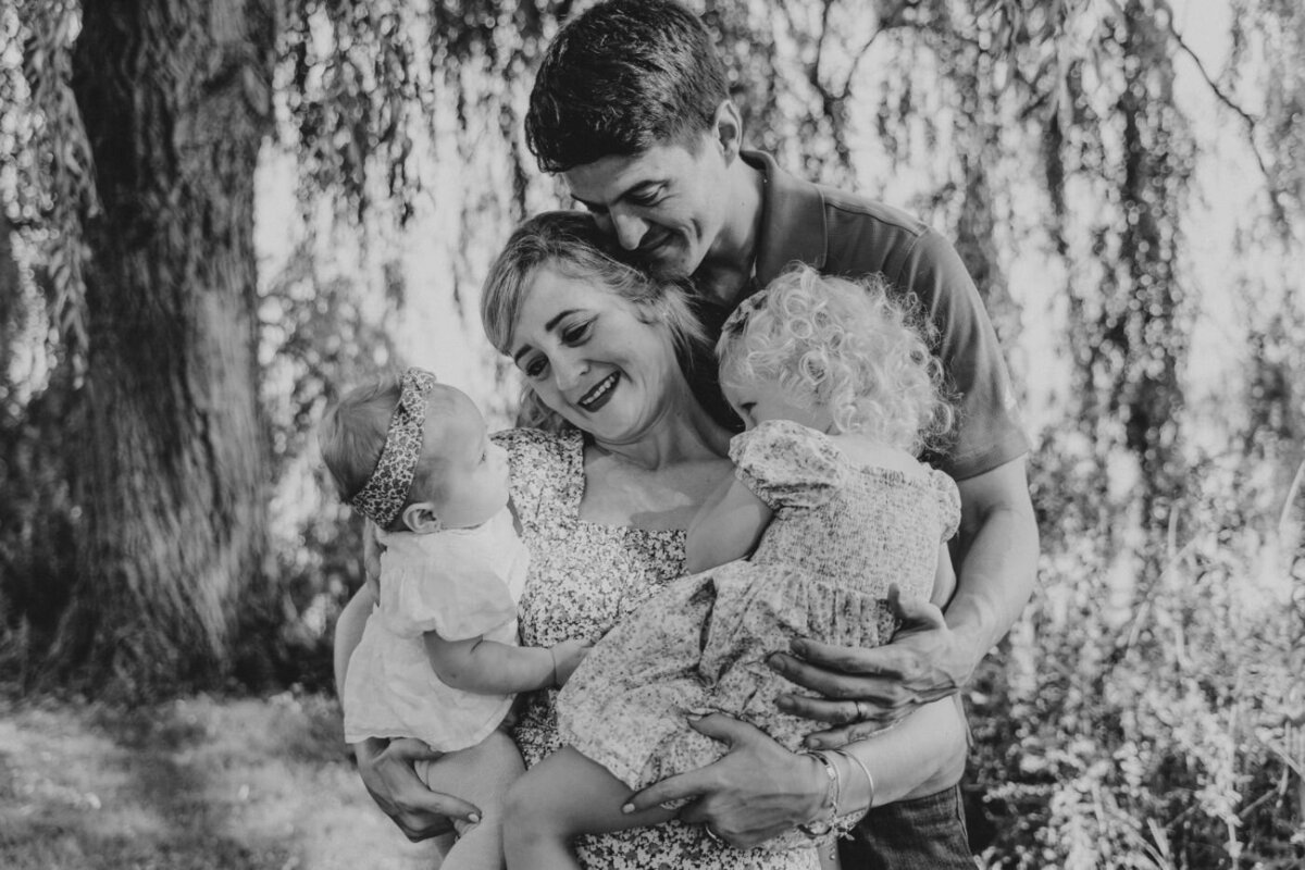 Black and white photo of parents embracing their two young daughters under trees.