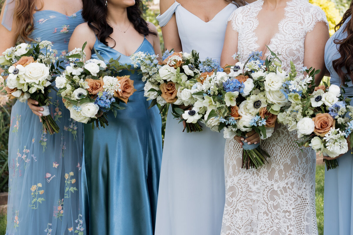 Bridesmaids hold stunning floral bouquets with white, blue, and peach flowers, complementing their dresses.