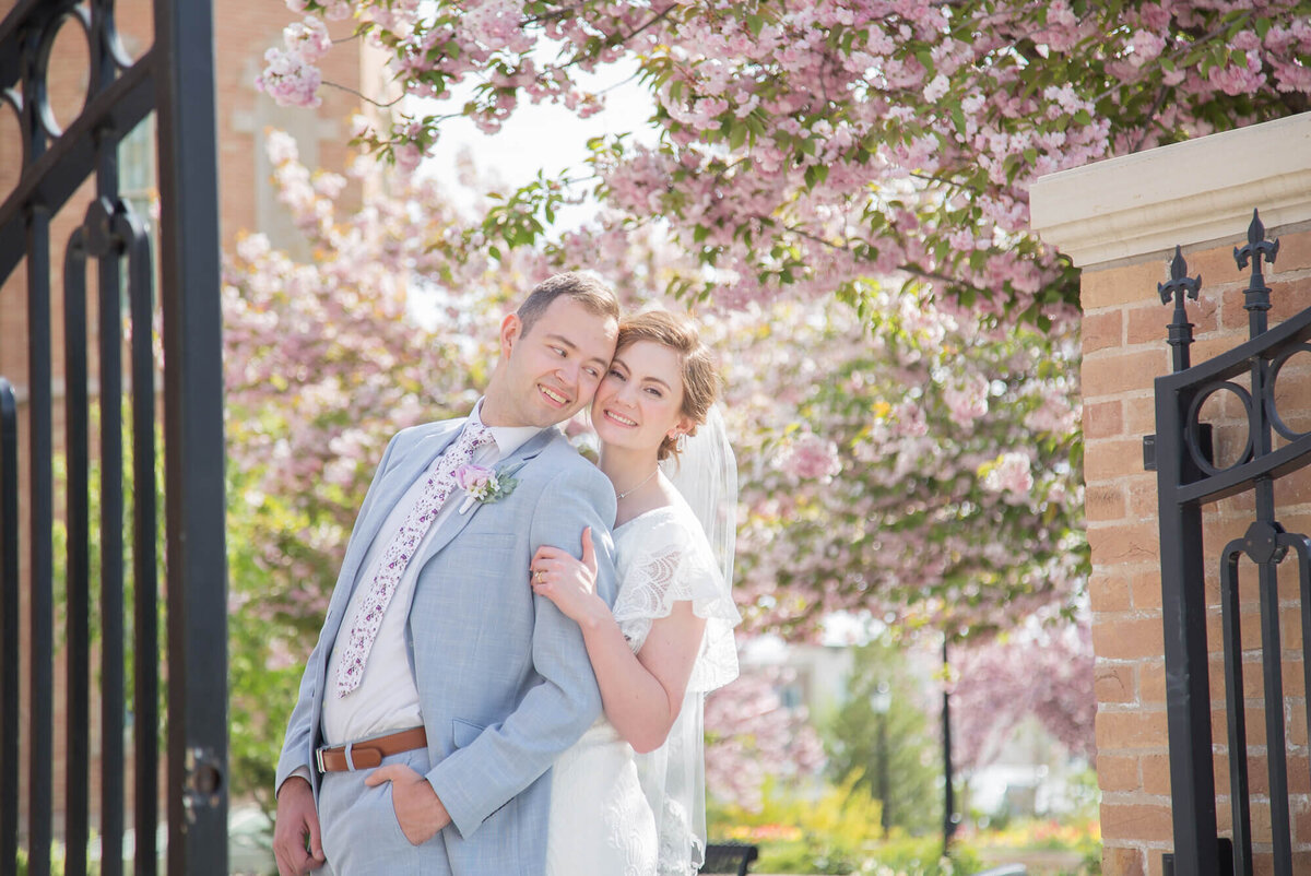 a wedding couple leaning into each other in front of spring blossoms