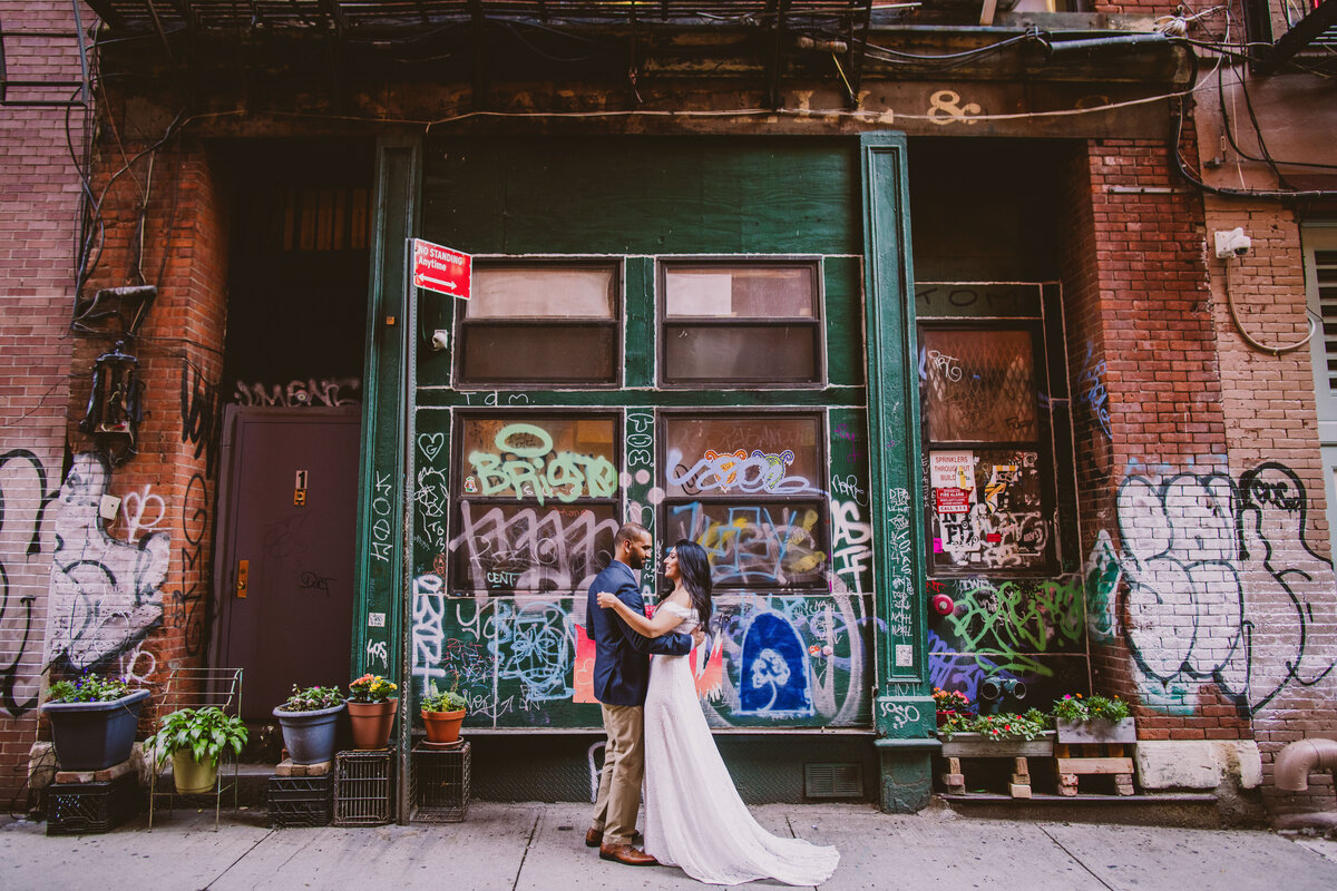 A couple during their engagement session embrace on staple street in tribeca in front of a graffiti building in nyc