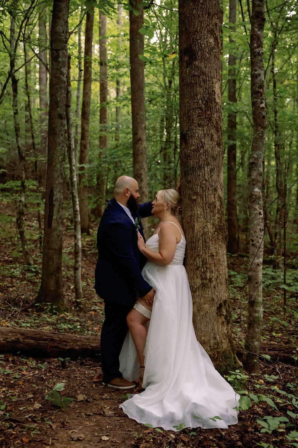 intimate moment with couple eloping to gatlinburg in the woods with woman leaning against a tree as her groom leans into her.