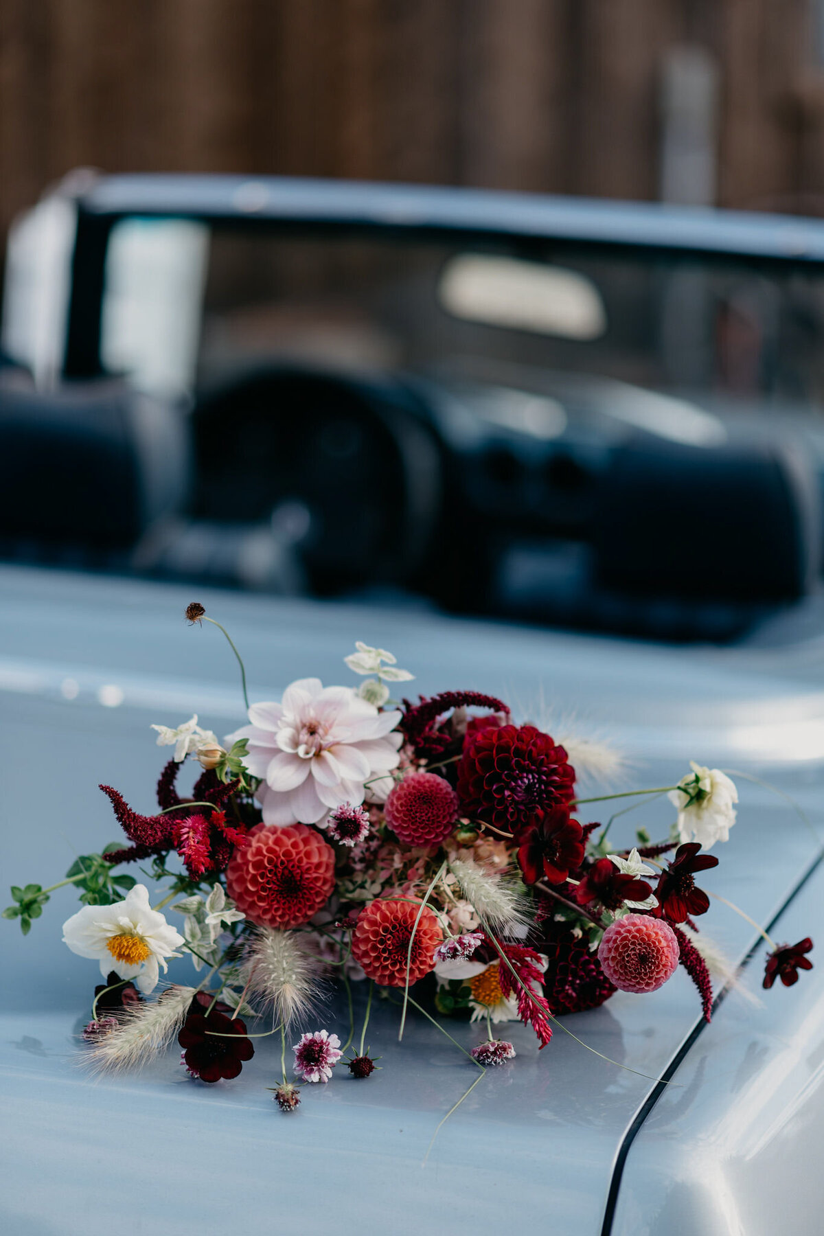 A moody bridal bouquet of lush dark flowers sits on a car at a Montreal wedding.