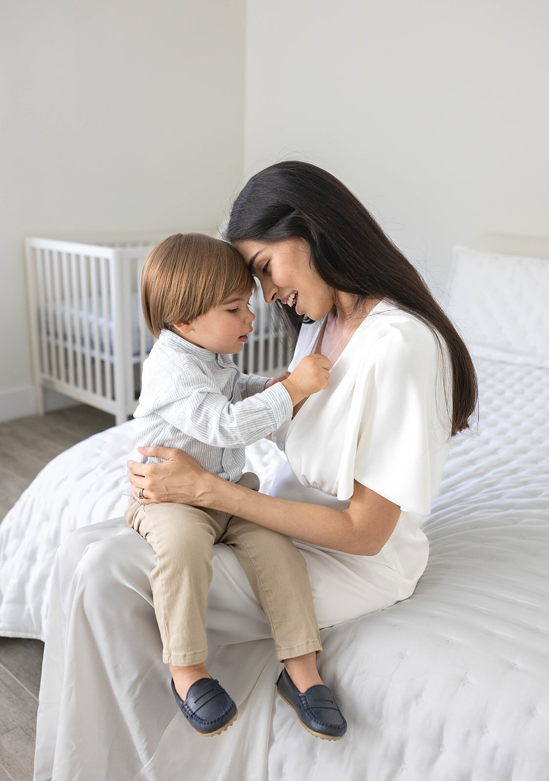A mother shares a sweet moment with her young son in a bright, cozy bedroom during a Florida Keys family portrait session.