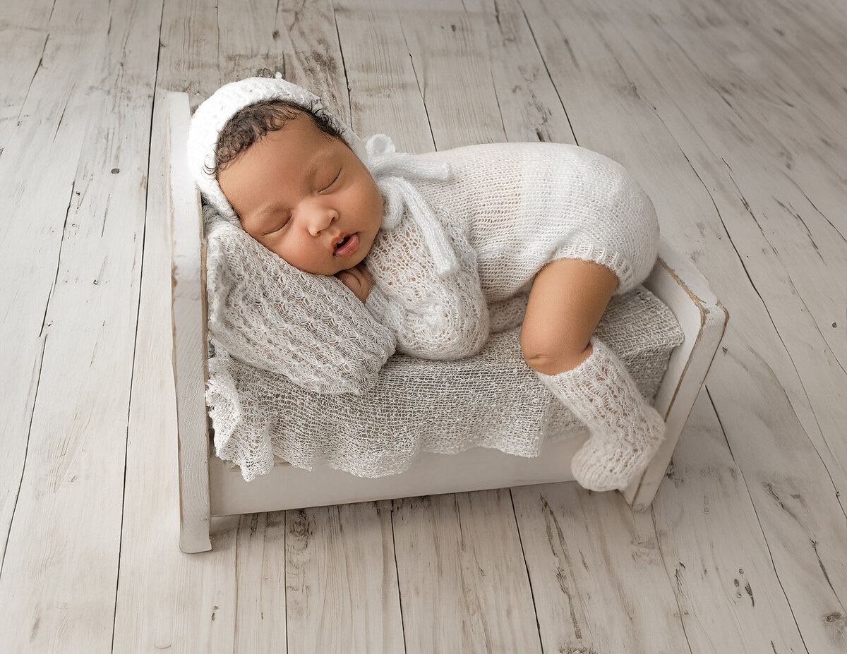 sweet baby girl wearing all white rests in a little wooden bed during her newborn photography session in Haldimand County