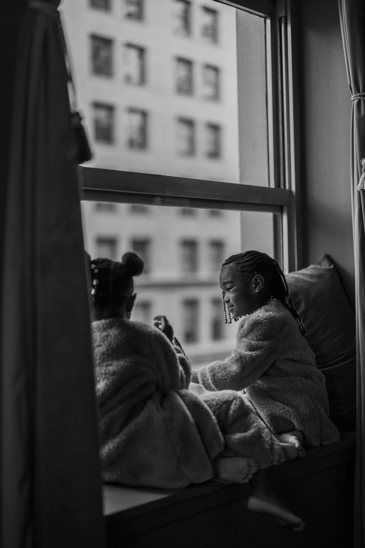 A serene moment of siblings sitting together by a window, bathed in natural light, capturing a timeless family scene during an NYC session.