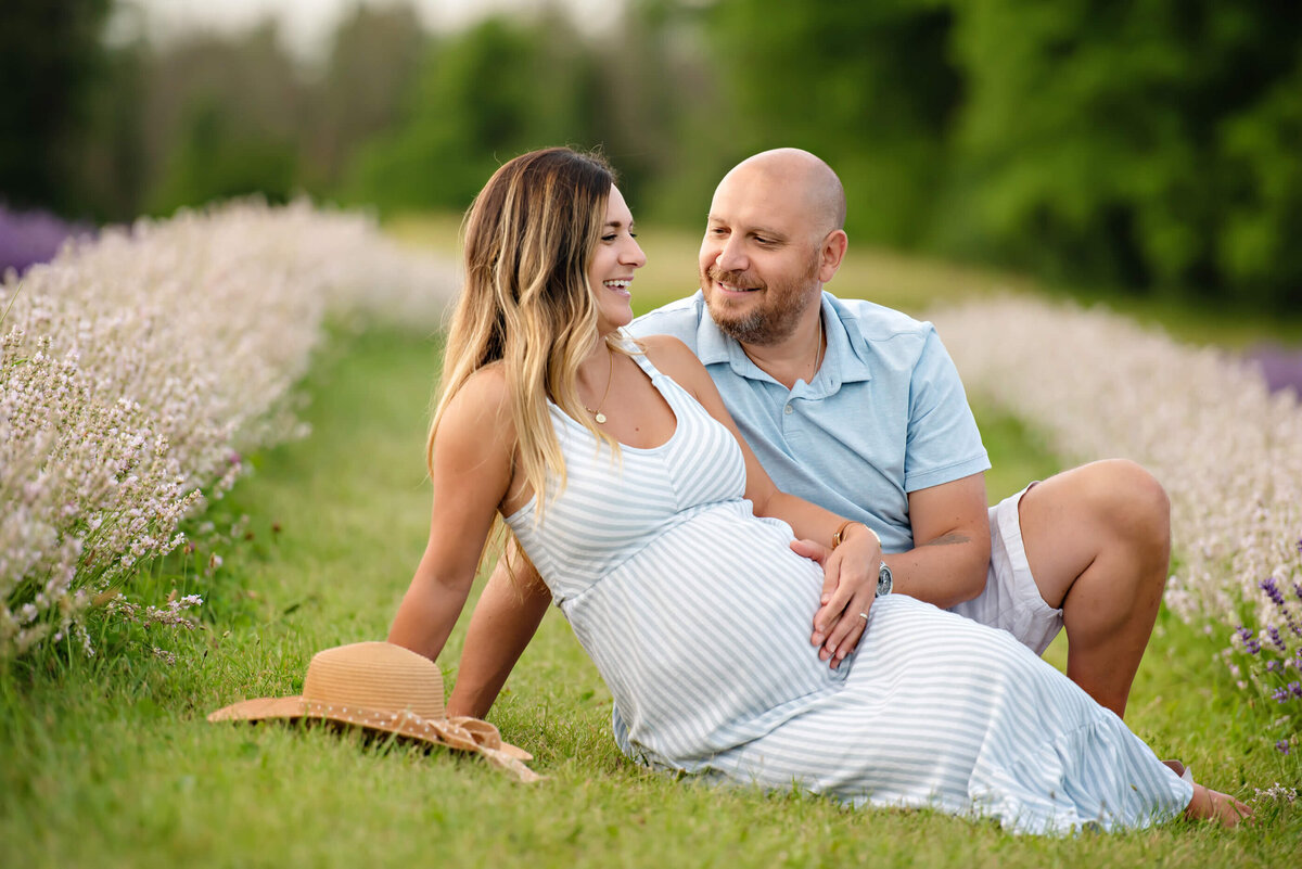 mom and dad sitting on the ground in the lavender field for their maternity photos