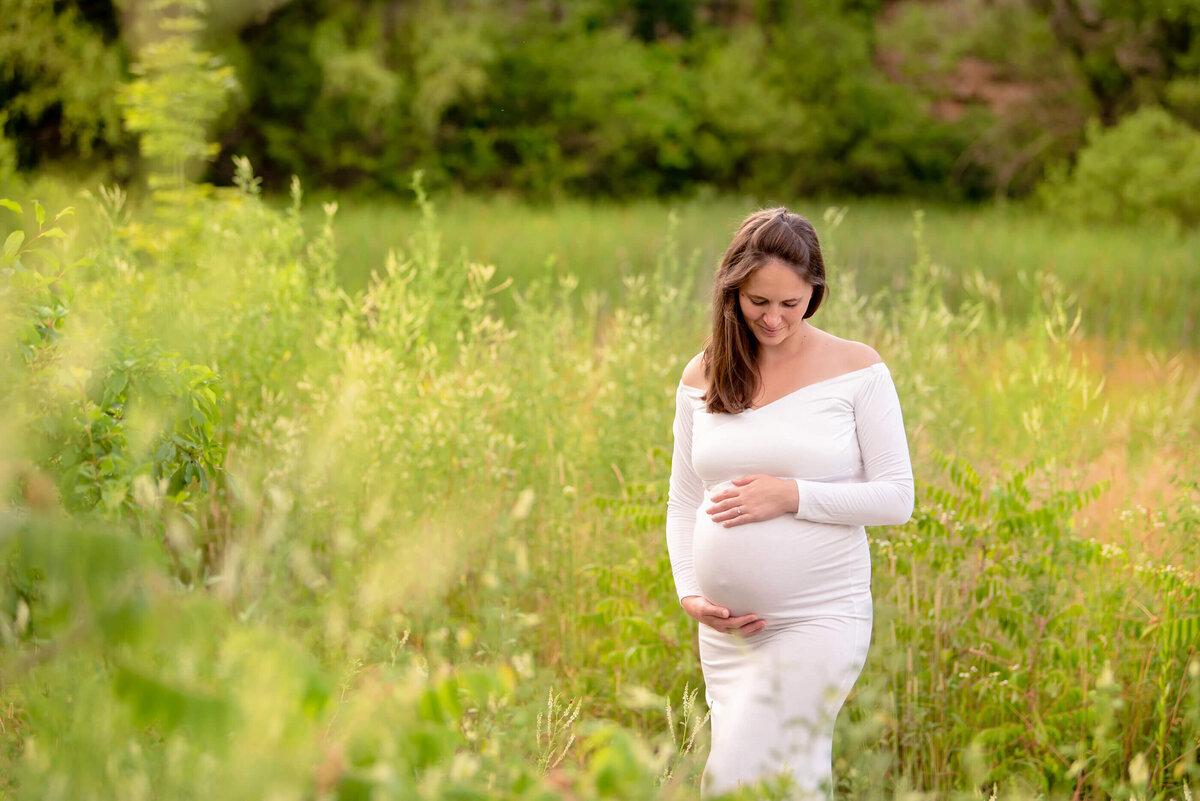 pregnant woman holding her belly in a field for her Burlington outdoor maternity photography session