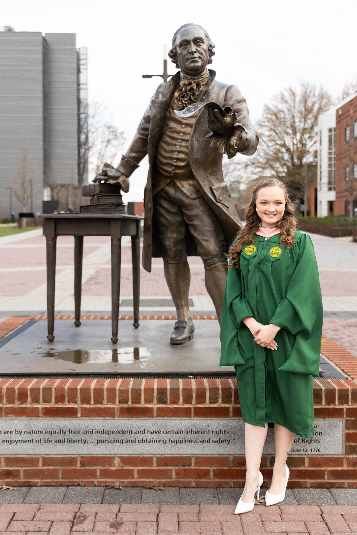 George Mason Graduate in front of George Mason Statue smiling in her graduation gown