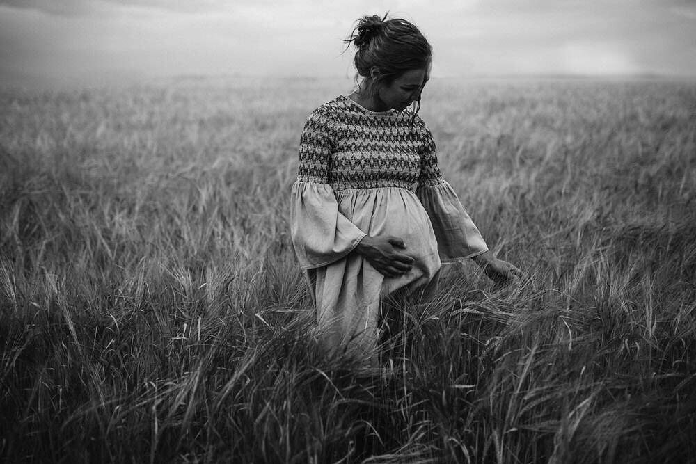 Pregnant woman stands in a feild of wheat whilst holding her belly