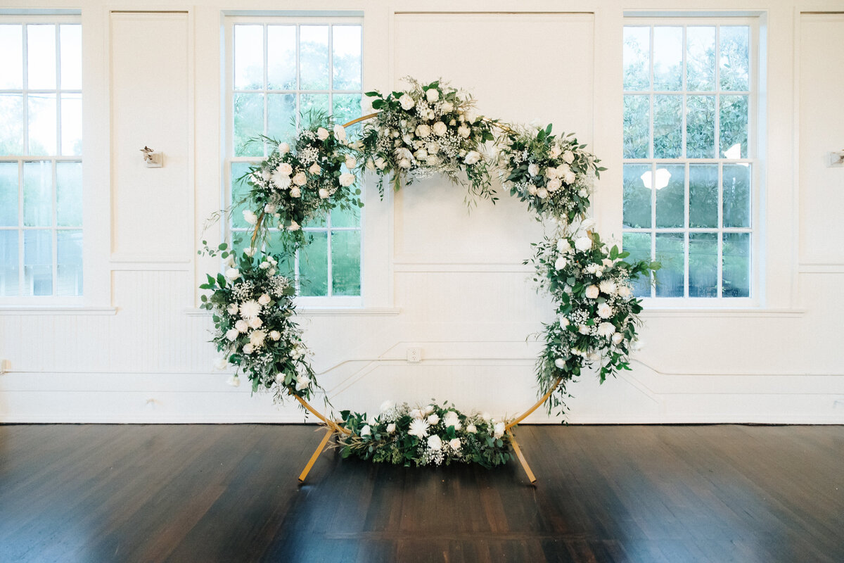 Golden round metal arch covered with clumps of white flowers and greenery.