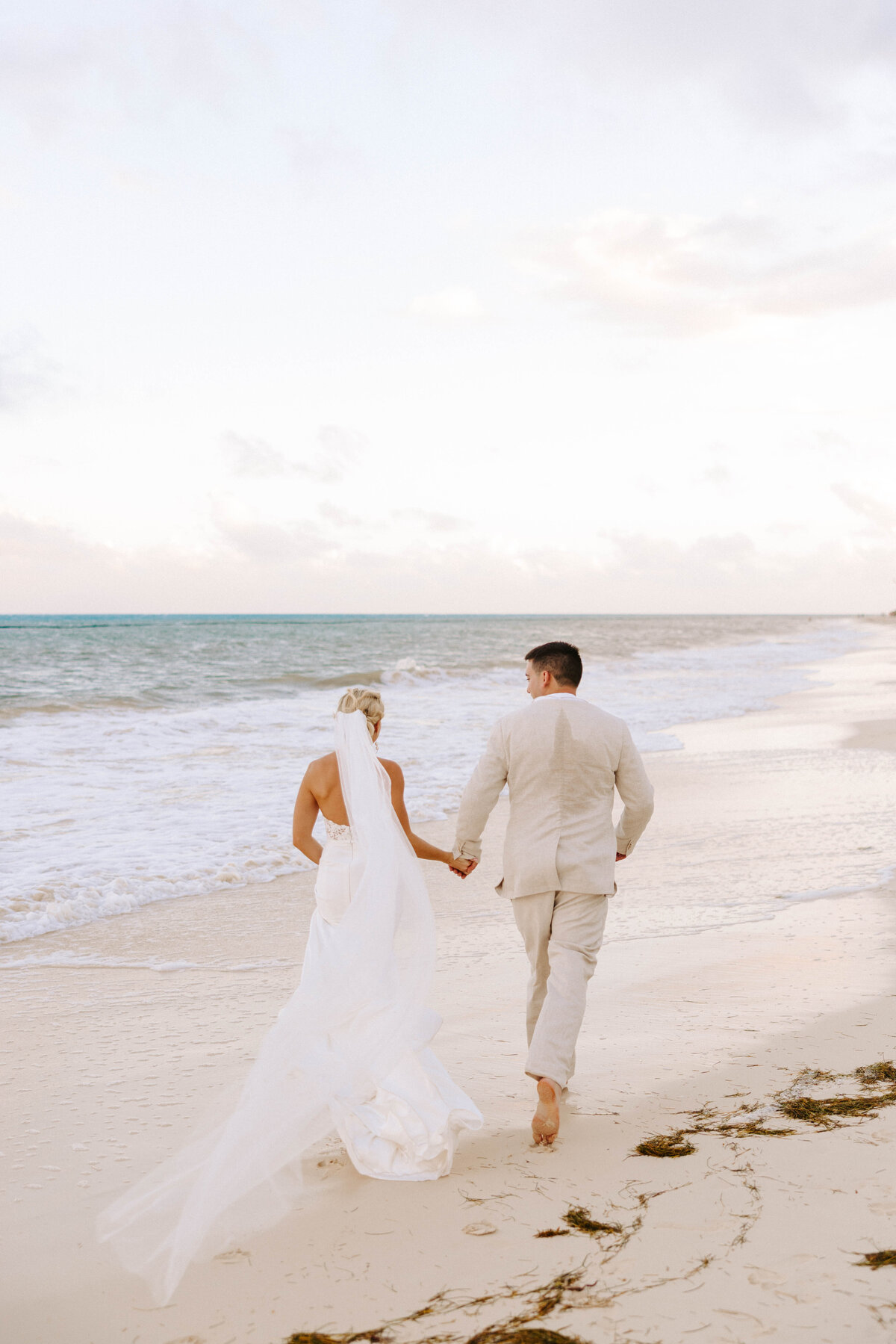 bride and groom walking, holding hands, down the beachside Cancun, Mexico