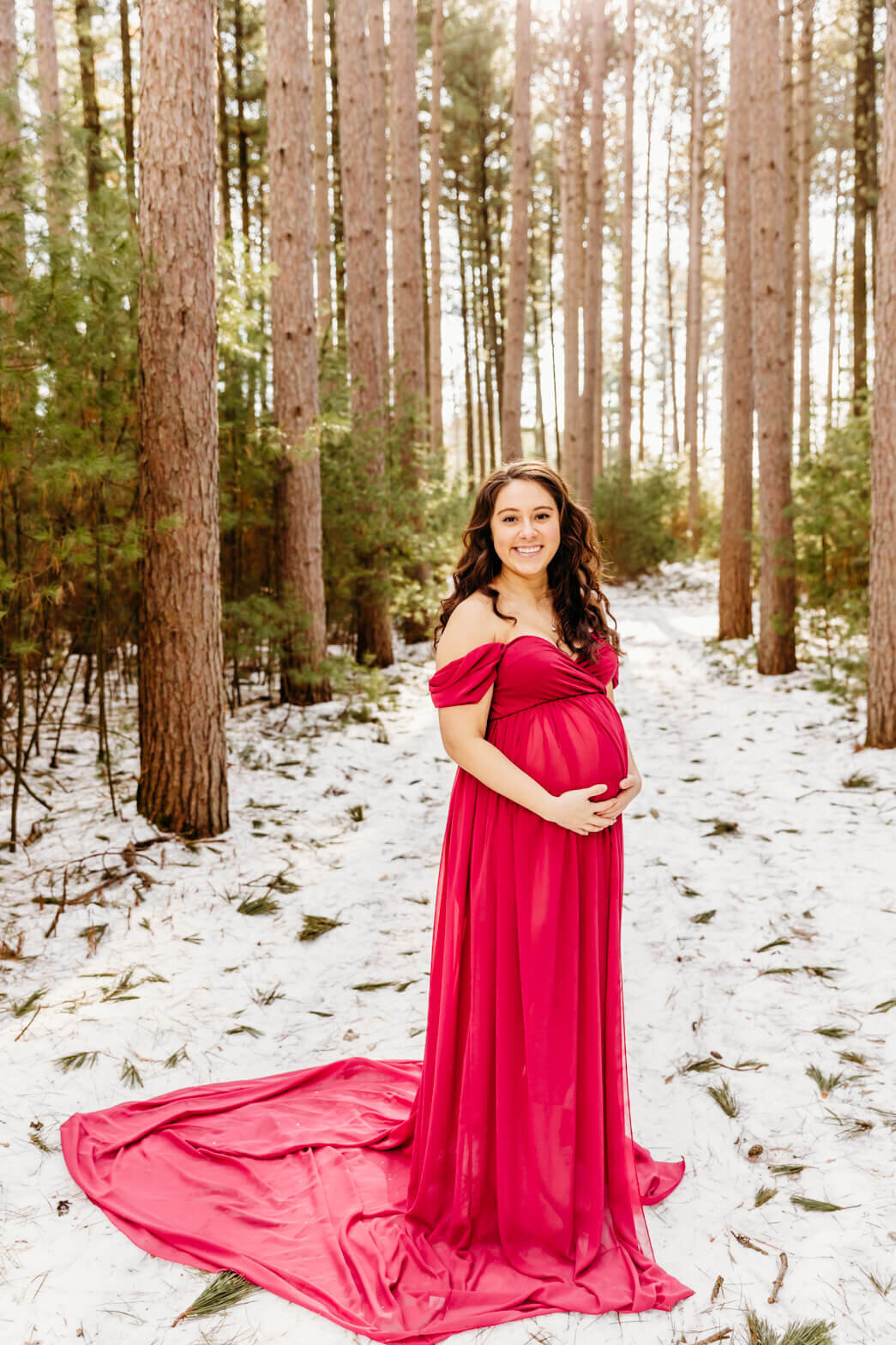 beautiful pregnant mother in a gorgeous pink gown holding her bump in a snowy forest  by Ashley Kalbus