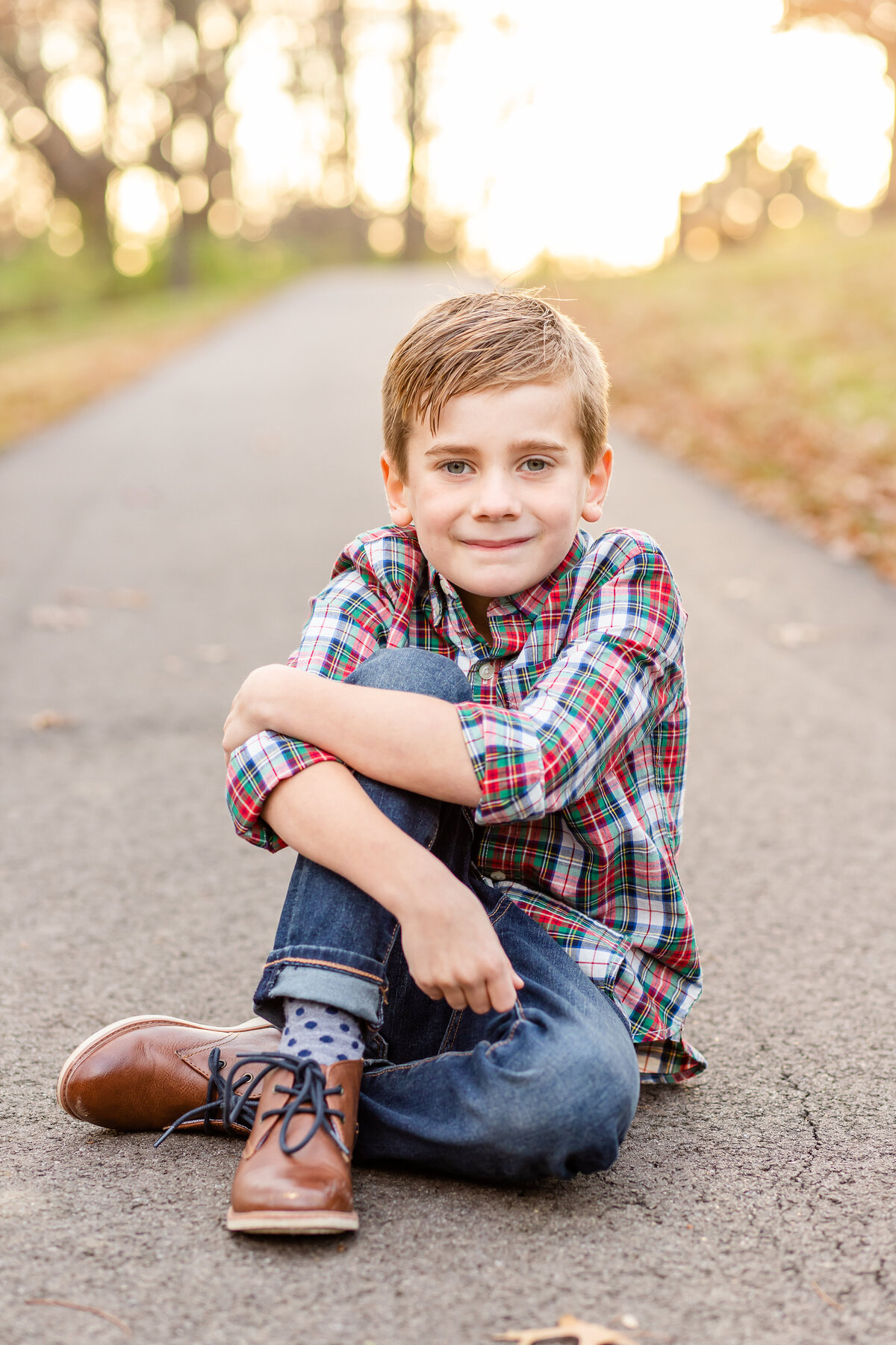 Young boy sitting with legs crossed on park pathway