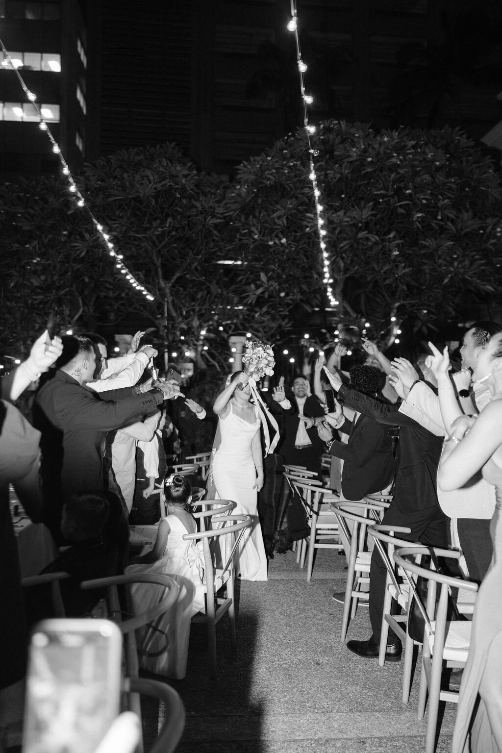 Bride and groom grand entrance walking through all of their guests cheering in black and white