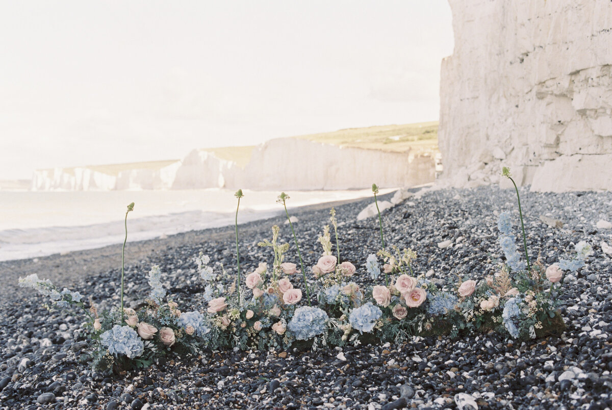 blue hydrangea and pink roses grounded flower arch displayed on the beach rocks and beach on the background