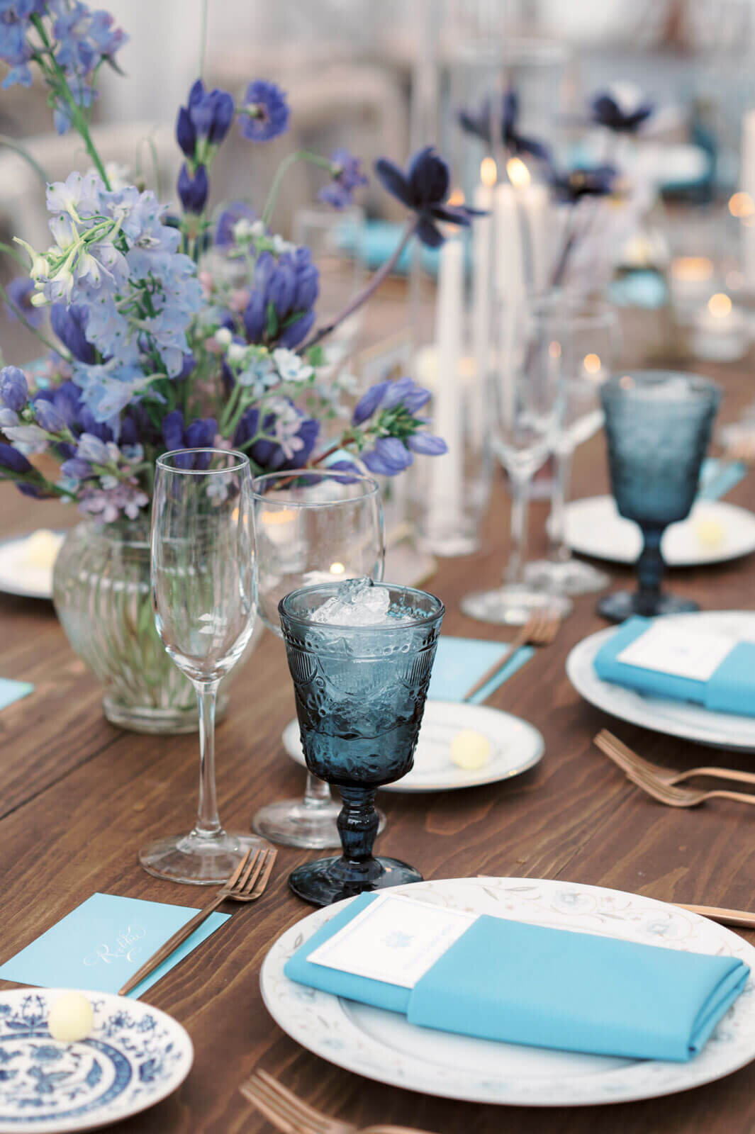 An elegant wedding reception dining table with flowers, napkins, and wine glasses in shades of blue at The Ausable Club, NY. Image by Jenny Fu Studio