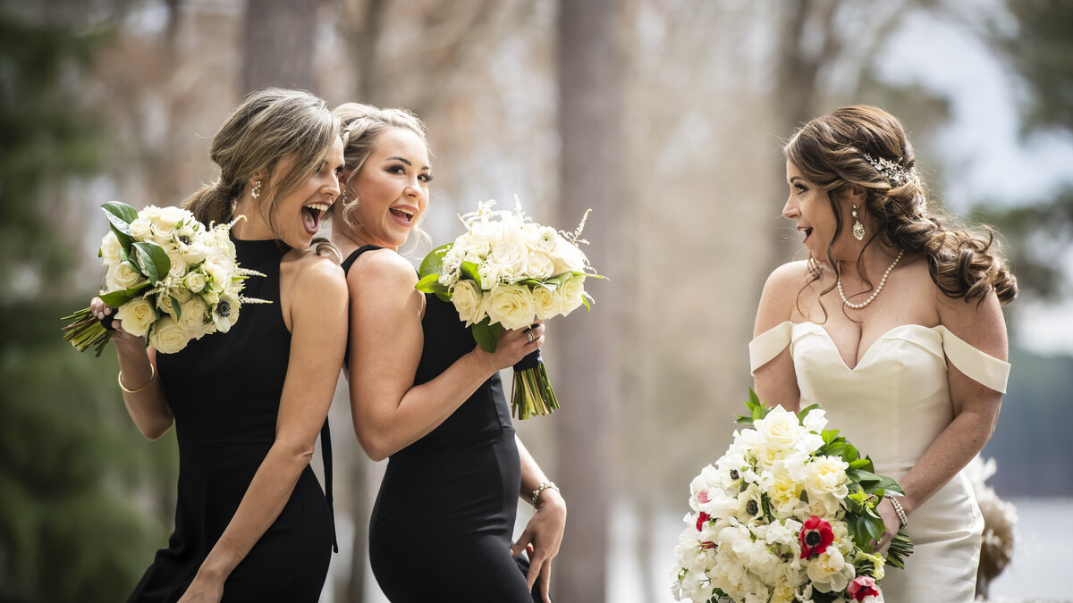 Bridesmaids in black dresses making bride laugh.