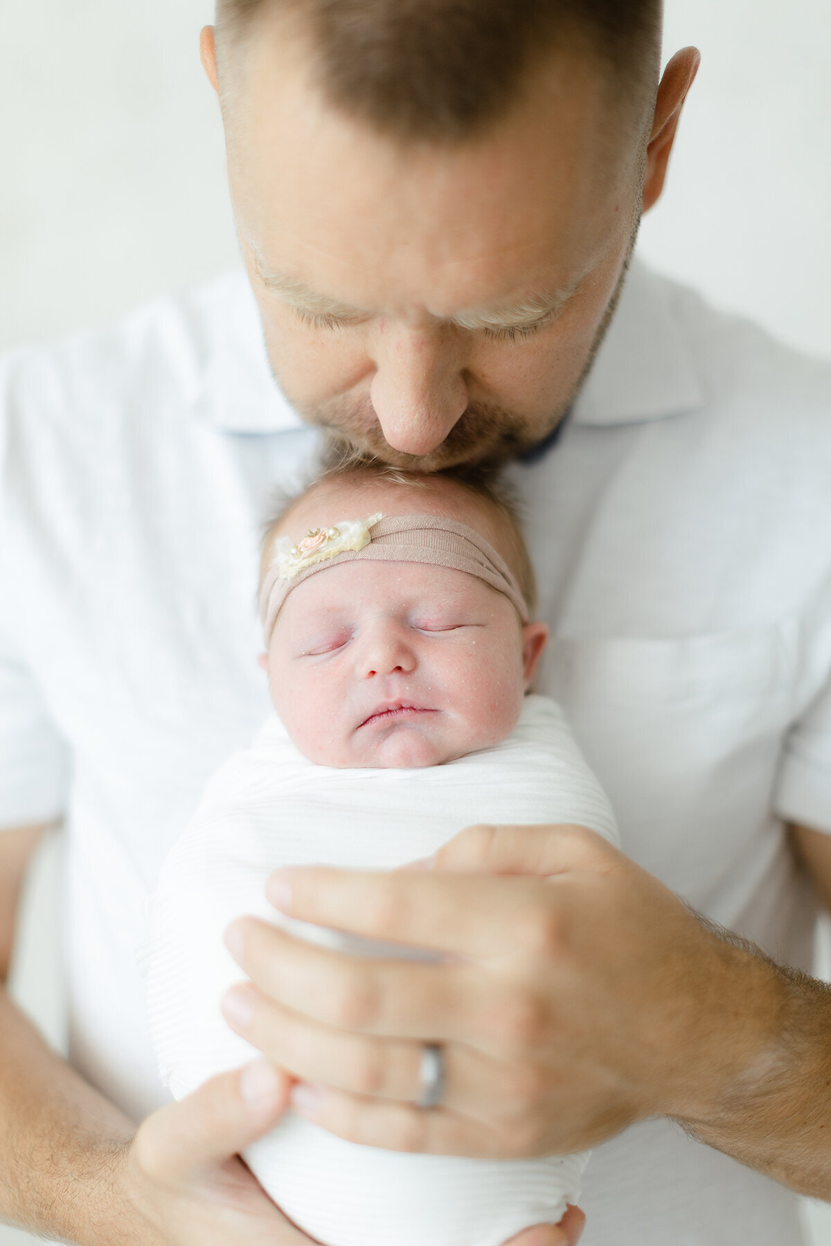 Newborn photo of a father holding his newborn baby girl up as he kisses her head.