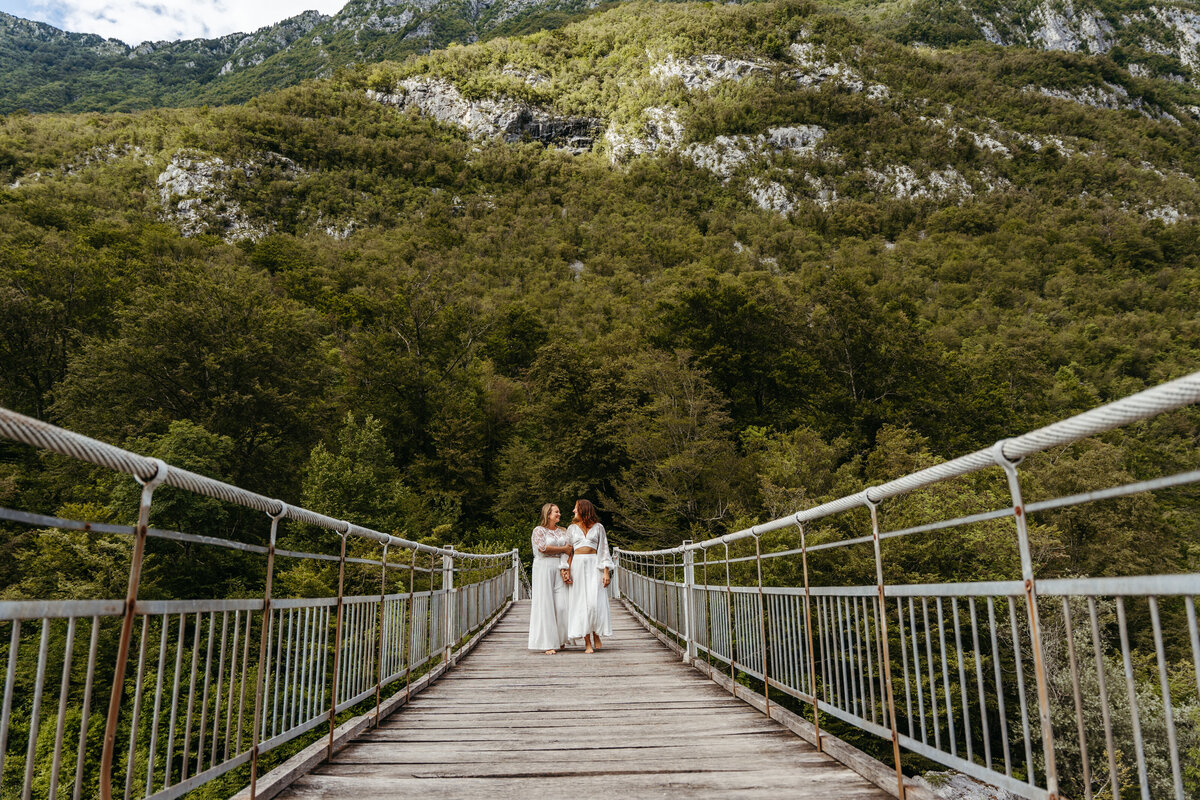 Same-sex elopement kiss on mountain river bridge