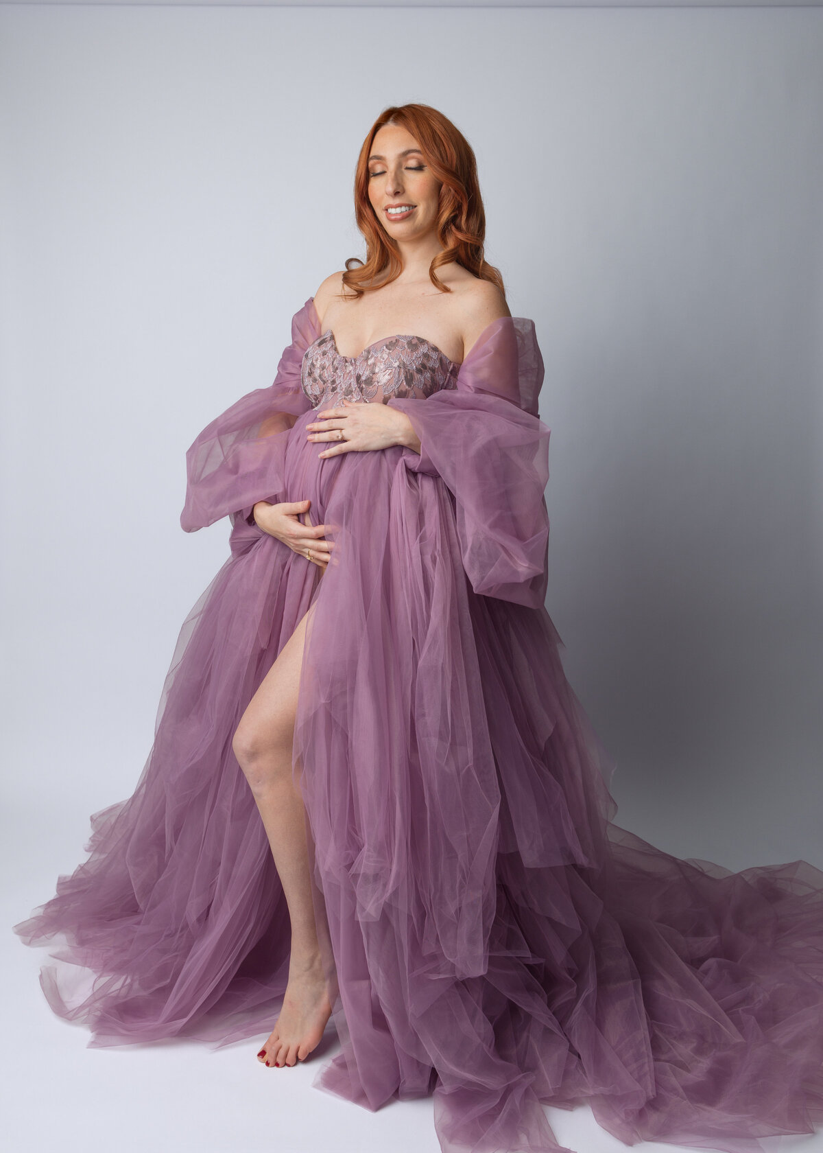 Elegant pregnancy portrait in a flowing mauve tulle gown against a light gray backdrop. Bergen County Maternity Photographer.