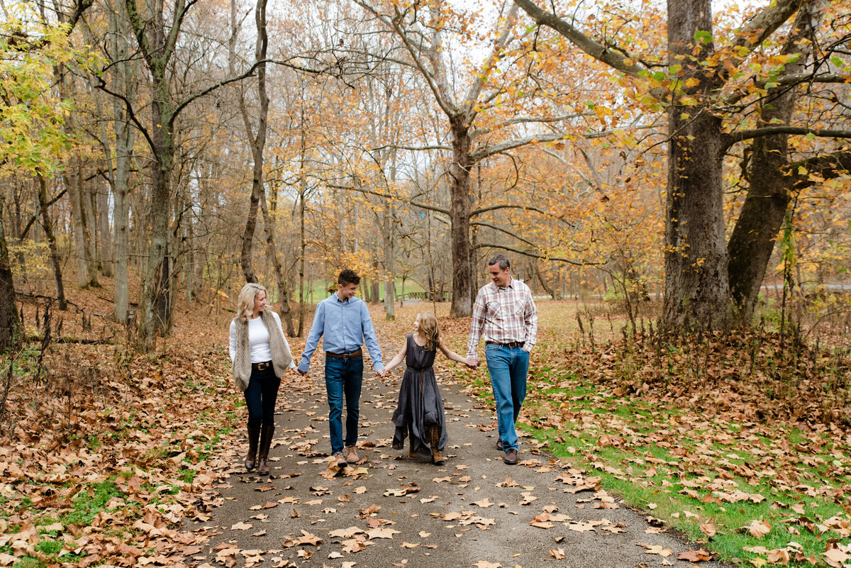 family members hold hands and walk along path at park