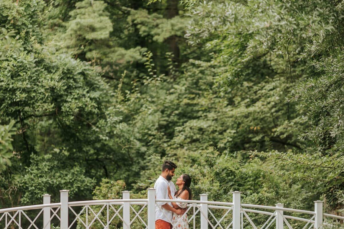 Couple hold each other on bridge surrounded by greenery in New Jersey.