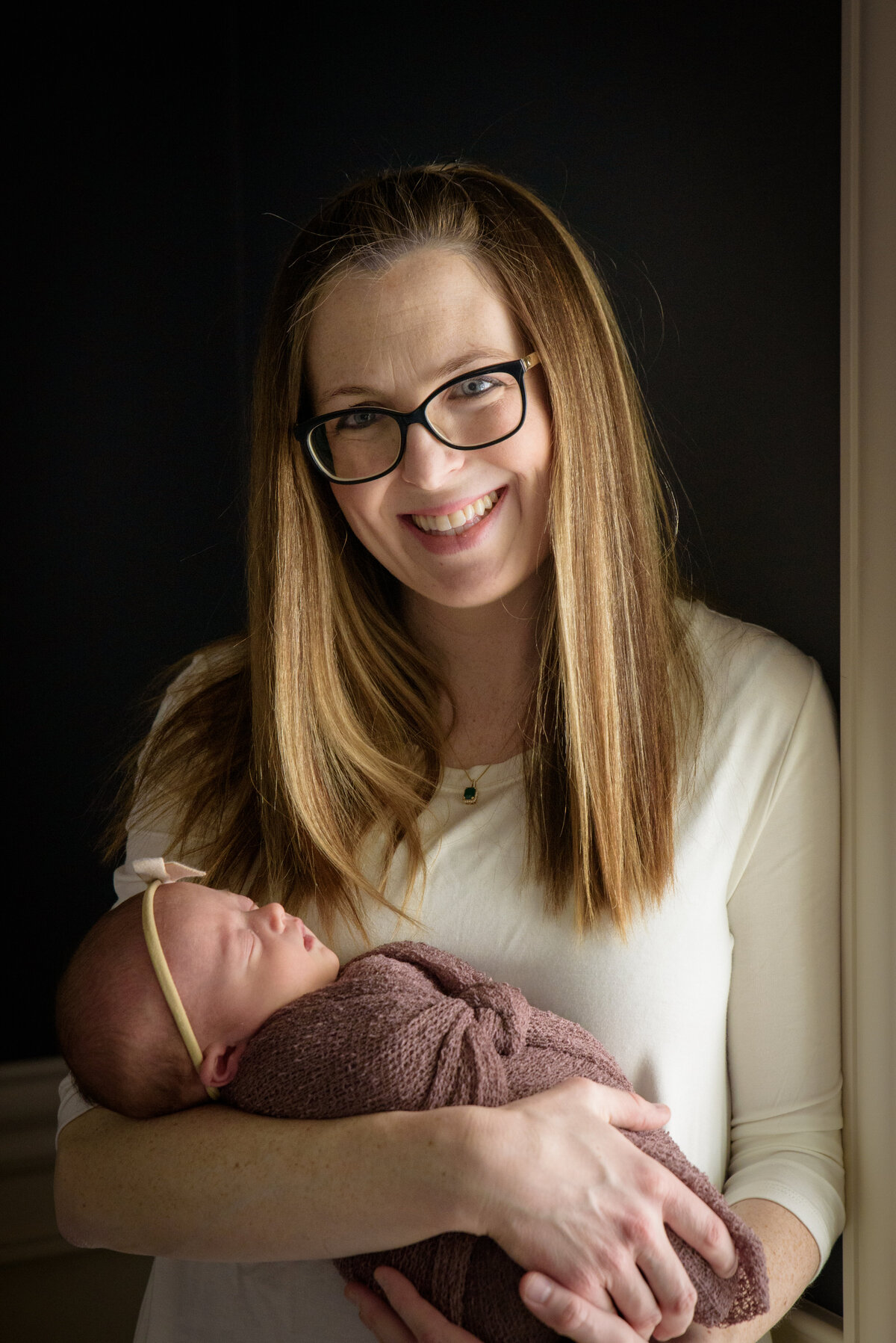 Beautiful mother holding new baby girl in a dusty rose wrap in natural light in their home in Green Bay, Wisconsin.