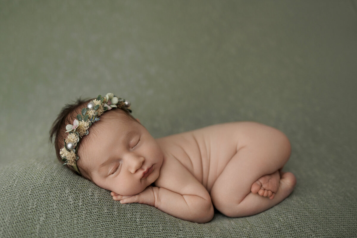 Newborn baby peacefully sleeping on a green blanket, adorned with a delicate floral headband.