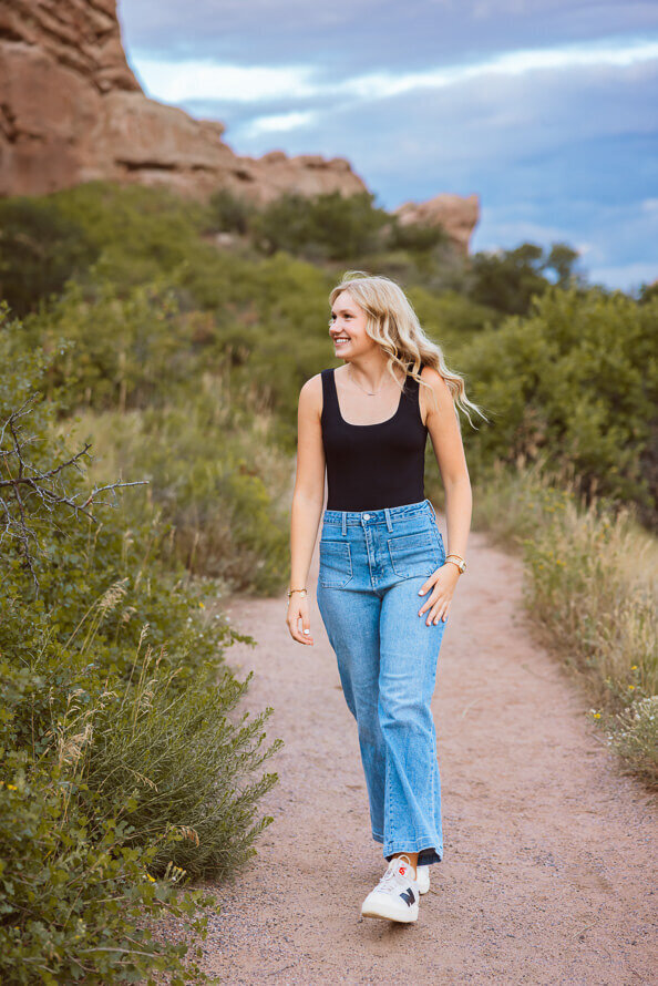 Girl laughs at something off to the side while walking on a trail with green bushes on the side.