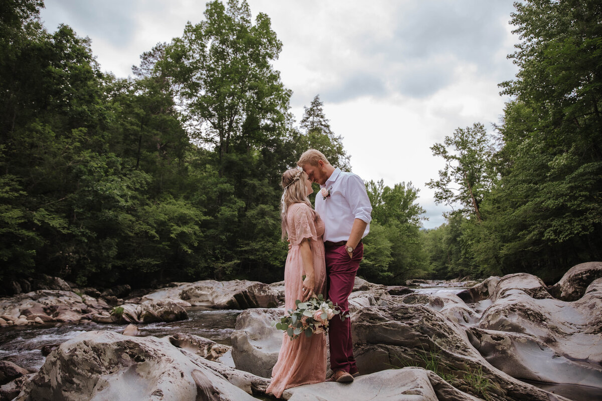 outdoor summer wedding with bride and groom leaning into each other while posing on large boulders in the woods of the smoky mountains